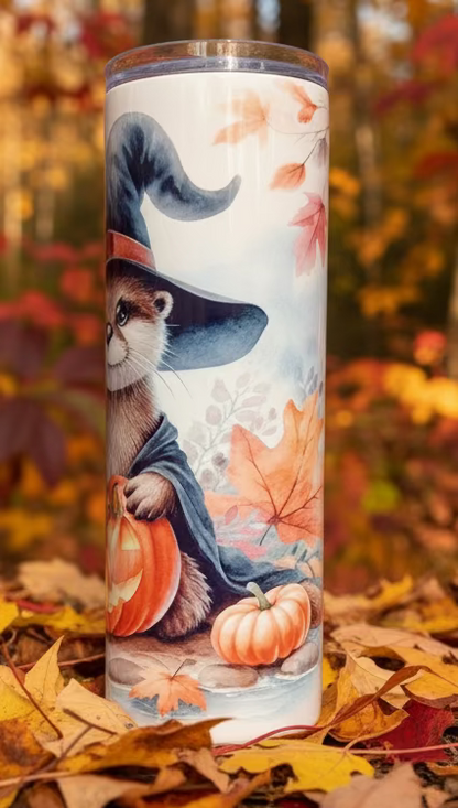 Tumbler with autumn-themed design featuring a otter in a witch hat, pumpkins, and leaves on a white background.